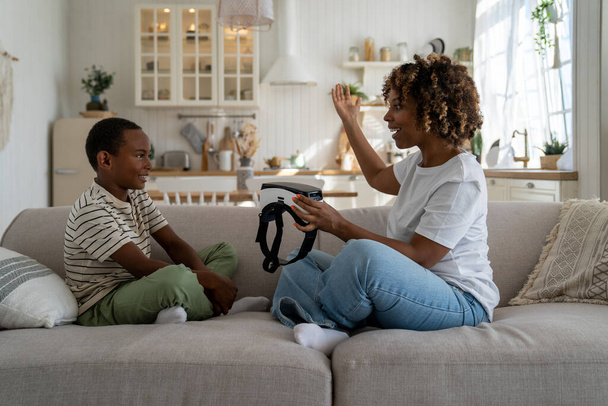 Jovem excitada afro-americana mãe falando com filho criança sobre aplicativos educacionais de RA e VR para crianças, mãe segurando óculos de realidade virtual introduzindo nova tecnologia futura para criança - Foto, Imagem