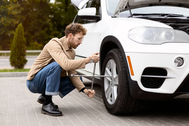 Attractive man replacing wheel in car, twisting it with wrench. Concept of car repair, wheel replacement - Foto, Imagem