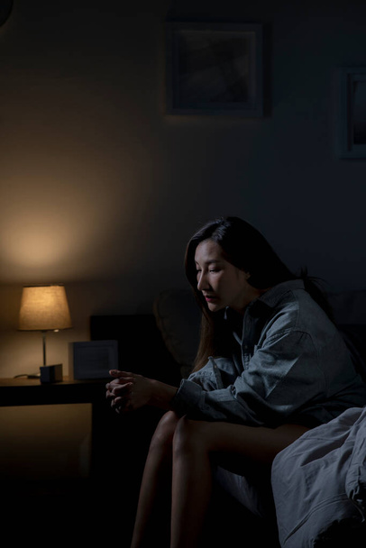 Молодая азиатка в спальне чувствует себя грустно усталой и обеспокоенной страдающей депрессией в психическом здоровье, женщина сидит в постели не может спать от бессонницы. - Фото, изображение