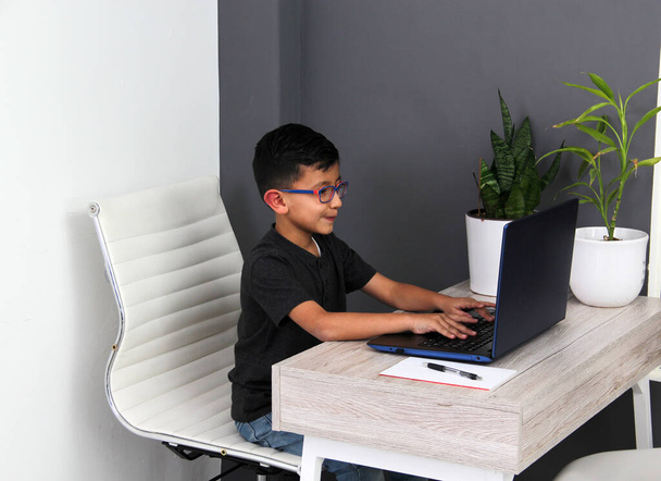 7-річний латиноамериканець з окулярами проводить домашню освіту вдома на столі з ноутбуком, вчиться, дивується і бере участь у класі. - Фото, зображення