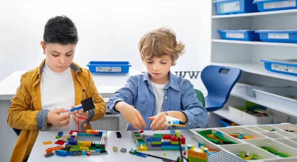 Robot programlama dersi. Çocuklar robot yapıp kodluyorlar. İnşaat blokları, dizüstü bilgisayar ve uzaktan kumandalı joystick kullanarak STEM eğitimi. Okul çocukları için teknolojik eğitim gelişimi - Fotoğraf, Görsel