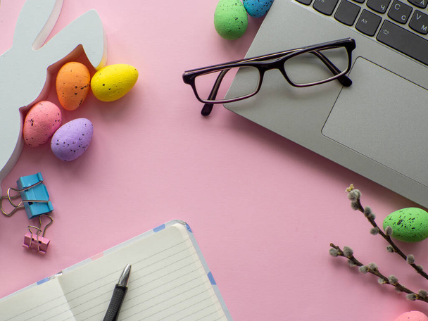 Easter work concept. Flat lay. Business work desk with devices and happy easter holiday multicolored eggs on pink background. Spring decoration workplace with gadgets. Work day on Easter holidays. - Foto, Imagem