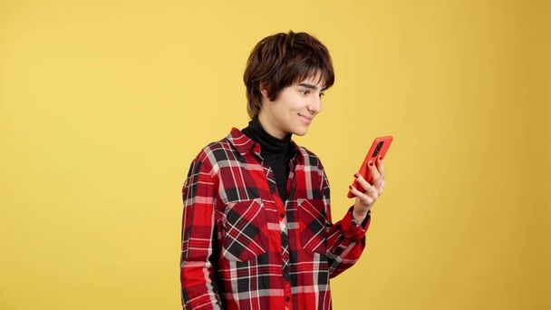 Androgynní osoba slaví při používání mobilu ve studiu se žlutým pozadím - Fotografie, Obrázek