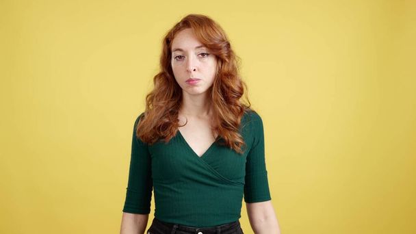 Redheaded woman looking at camera with an angry expression in studio with yellow background - Photo, Image