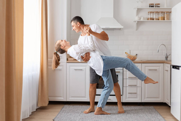 Happy loving young couple dancing on date in modern kitchen smiling husband and wife celebrating anniversary enjoying tender moment having fun. - Фото, зображення