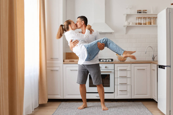 Attractive family man and woman having fun in kitchen celebrating relocating guy holding his girlfriend or wife and kissing expressing romantic feelings - Fotó, kép