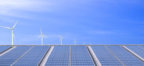 Vue panoramique de nombreux panneaux solaires photovoltaïques sur le toit de construction d'usine avec éoliennes sur fond bleu, concept d'énergie durable et renouvelable - Photo, image