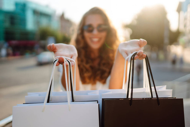 Happy stylish woman with shopping bags enjoys sunny weather walking down the street. A young woman with shopping goes from the mall. Summer shopping. The concept of lifestyle, shopping, selling. - Foto, Bild