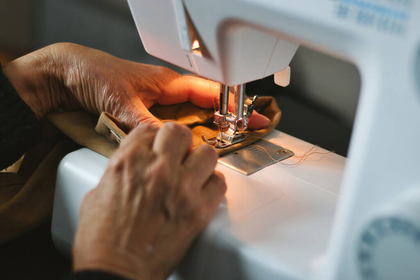家庭用ミシンで糸を素材に縫いつける老婦人の手のクローズアップ - 写真・画像