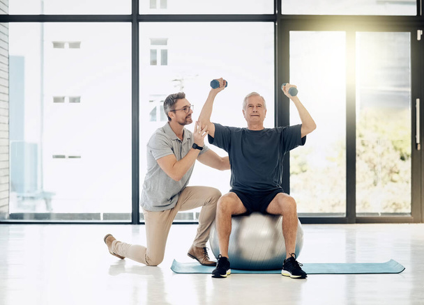 Hes getting a little stronger with every session. a friendly physiotherapist helping his mature patient to use dumbbells in a rehabilitation center - Foto, Imagen
