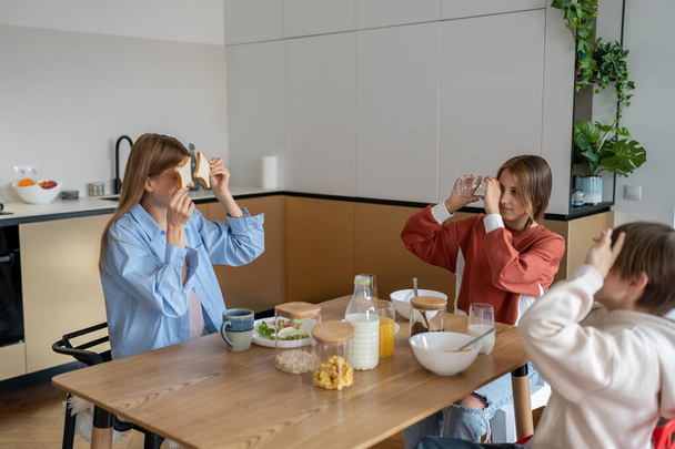 Joyful caucasian family young mother and two kids having fun during breakfast at home, bonding and enjoying morning time together at home. Mom enjoy early hours with children before school - Фото, зображення
