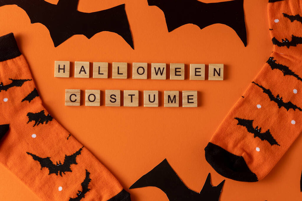 Orange socks with bats. Clothing costume for Halloween costume party. Cheerful bright multicolored sock top view. Phrase in wooden letters. Word. - 写真・画像