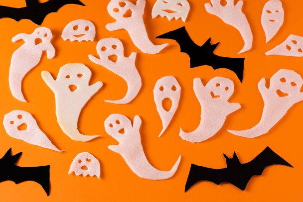 White ghosts and bat craft for Halloween party. Wrapping paper ghost on orange background top view. Cartoon creepy Whisper. DIY hand made. Set boo characters. - Foto, immagini