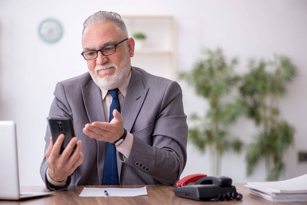 Old employee speaking by phone at workplace - Photo, image