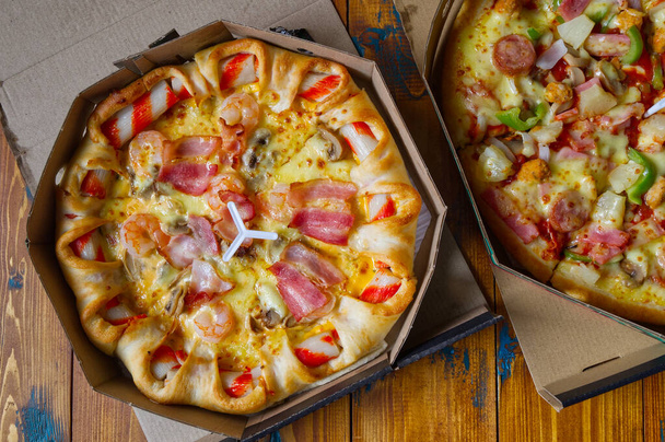 Pyszna pizza serwowana w pudełku na drewnianym stole, włoska pizza w pudełku tekturowym. - Zdjęcie, obraz