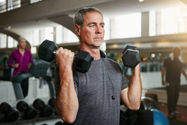 Je bent nooit te oud om op te tillen. een senior man die traint met gewichten in de sportschool - Foto, afbeelding