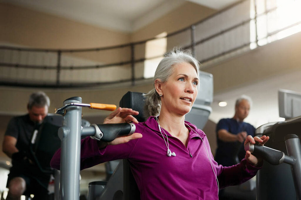 Nechť je stárnutí vaší motivací k uzdravení. Portrét starší ženy, jak cvičí s hrudním lisem v tělocvičně - Fotografie, Obrázek