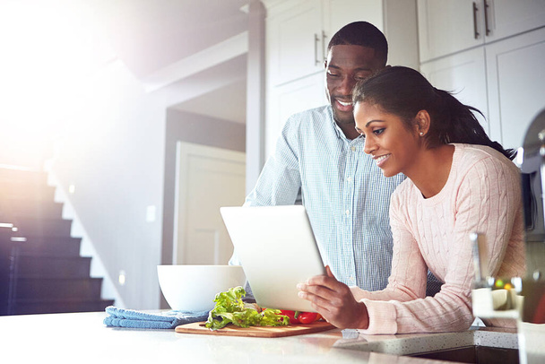 Digitizing the cooking experience. a young couple using a digital tablet while preparing a healthy meal together at home - Foto, imagen
