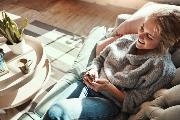 Vamos começar este fim de semana. uma jovem mulher relaxando no sofá em casa e usando um telefone celular - Foto, Imagem