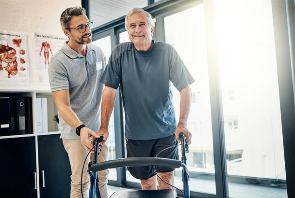 Jeder Schritt ist eine Erfolgsgeschichte. ein fürsorglicher Physiotherapeut, der seinem mündigen Patienten hilft, im Reha-Zentrum einen Rollator zu benutzen - Foto, Bild