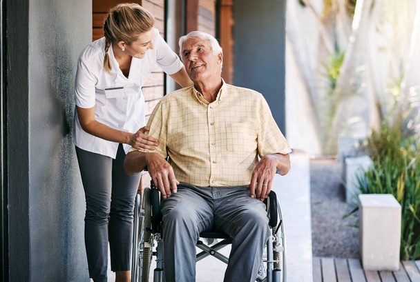 ¿Estás seguro de que estás lo suficientemente cómodo? una enfermera que cuida a un paciente mayor en silla de ruedas fuera de un hogar de ancianos - Foto, imagen