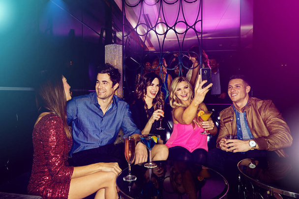 Las noches divertidas hacen recuerdos increíbles. un grupo de amigos tomando selfies en un teléfono móvil en una discoteca - Foto, Imagen