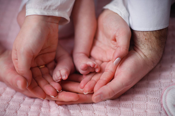 Le mani della madre e del padre tengono i piedini del bambino tra le palme, primo piano senza volti - Foto, immagini
