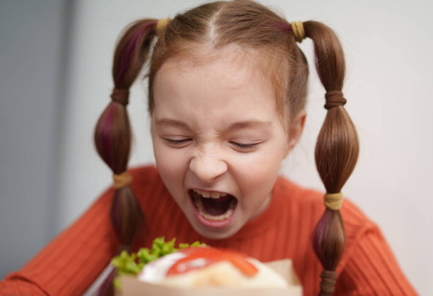 Funny white girl biting a sandwich. Portrait of cute 9 year old kid eating a pita souvlaki snack in a Greek fast food restaurant - Fotó, kép