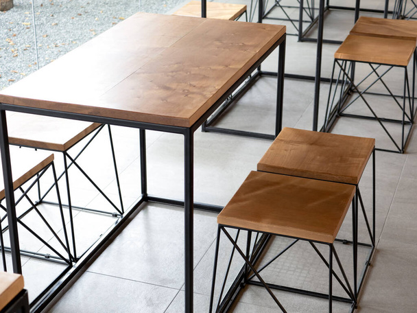 Prázdné dřevo dřevěný stůl set s židlemi na betonové dlaždice pozadí bez lidí, podkrovní styl kavárny interiér. Prázdný dřevěný nábytek s černou ocelovou výzdobou v betonovém přízemí v kavárně. - Fotografie, Obrázek