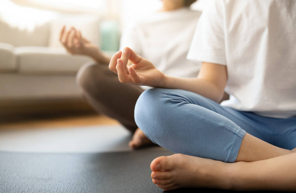 Teen european girl and millennial woman in sportswear sit in lotus position on mat, meditate, practice yoga in living room interior, cropped. Workout, sport, body care and health care at home - Foto, Imagen