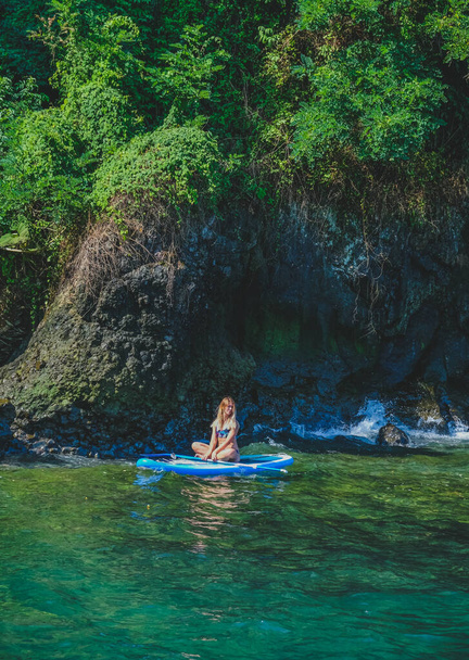 SUP Stand up peddelbord. Romantisch meisje op paddle board Uitzicht op het stenen strand en het groen. Blondine vrouw op zomervakantie levensstijl. Mtsvane Kontskhi Beach, Batumi, Georgië. - Foto, afbeelding