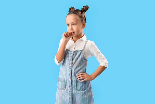 Little girl biting nails on blue background - 写真・画像