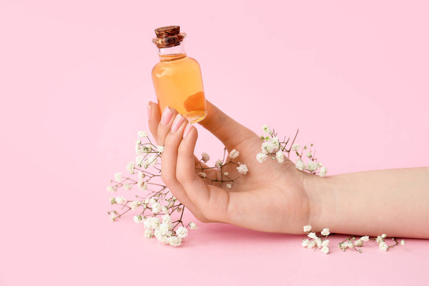 Nainen käsi pullo kynsinauhoja öljyä ja gypsophila kukkia värillinen tausta - Valokuva, kuva