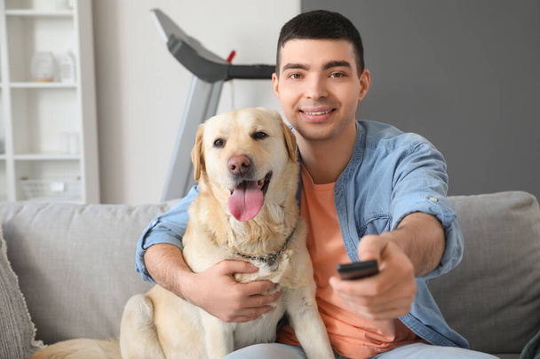 Νεαρός με χαριτωμένο Λαμπραντόρ σκυλί βλέποντας τηλεόραση στον καναπέ στο σπίτι - Φωτογραφία, εικόνα
