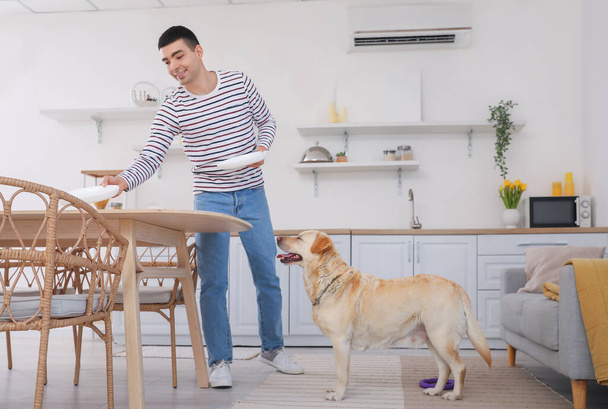 Giovane uomo con carino Labrador cane apparecchiare la tavola in cucina - Foto, immagini