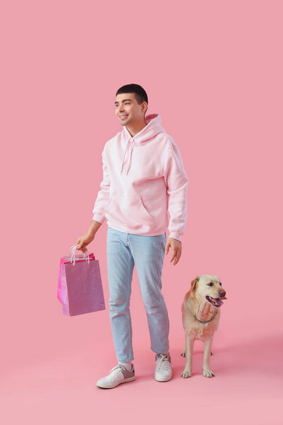 Νεαρός με τσάντες για ψώνια και Λαμπραντόρ σκύλος που περπατάει σε ροζ φόντο - Φωτογραφία, εικόνα