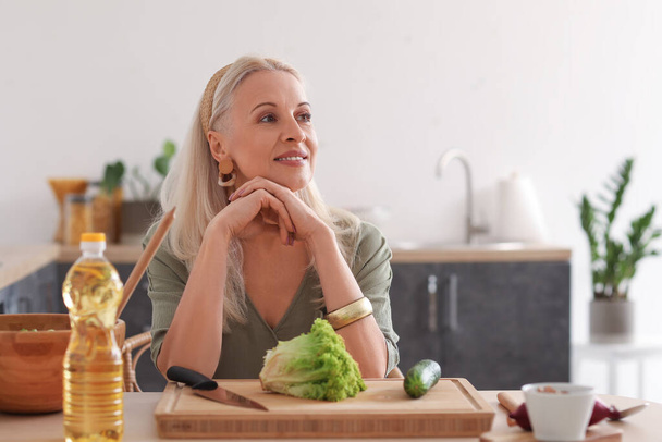Mulher madura fazendo salada de legumes à mesa na cozinha - Foto, Imagem