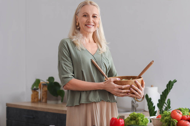 Femme mûre avec bol de salade de légumes dans la cuisine - Photo, image