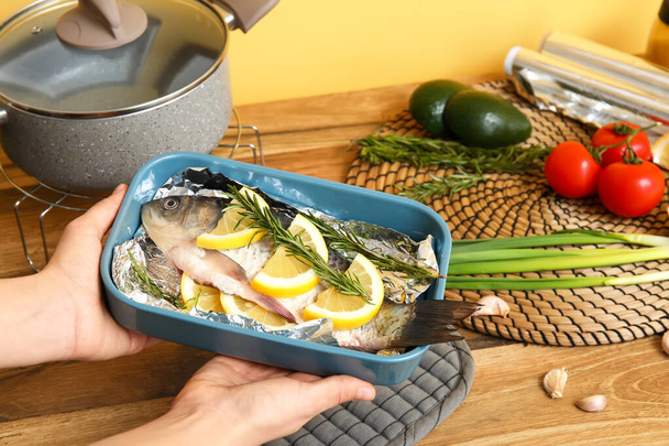 Frau hält Backform mit rohem Fisch und Gemüse in der Küche - Foto, Bild