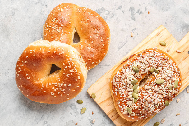 Wooden board of tasty bagels with sesame and pumpkin seeds on grunge background - Foto, immagini