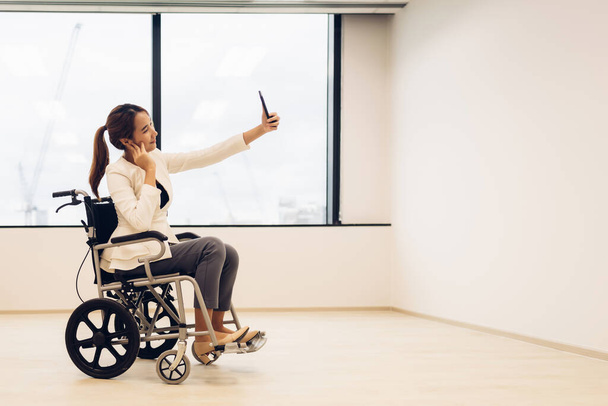 Office workers woman on a wheelchair in bright office and holding smart phone. - Zdjęcie, obraz