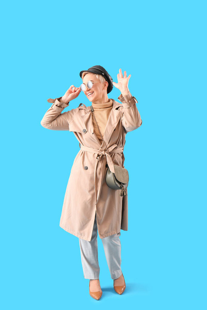 Stylish mature woman waving hand on light blue background - Zdjęcie, obraz