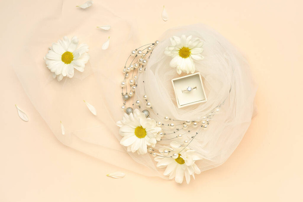 Box with engagement ring, necklace, daisy flowers and veil on beige background - Photo, Image