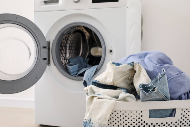 Cesta de lavanderia com roupas sujas e máquina de lavar roupa perto de parede leve no quarto - Foto, Imagem