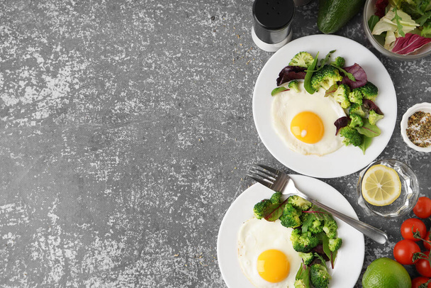 Plates with tasty fried eggs, broccoli and spinach on grey grunge background - Photo, Image
