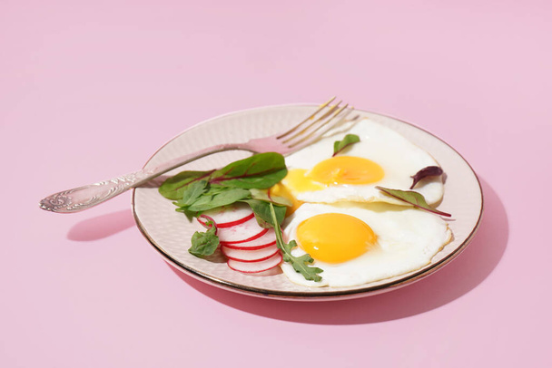 Placa con sabrosos huevos fritos, rábano y espinacas sobre fondo rosa - Foto, Imagen