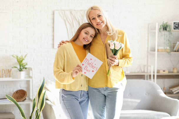 Jovem cumprimentando sua mãe com tulipas e cartão em casa - Foto, Imagem