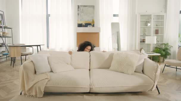 Glückliches Wochenende Konzept. Fröhliche Afroamerikanerin springt barfuß auf dem Sofa im modernen Wohnzimmer zu Hause. Glückliche Frauen feiern bewegenden Umzugstag und genießen neue Mietwohnung - Filmmaterial, Video
