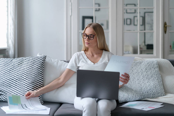 thoughtful female wearing glasses checking contract, girl remote employee engaged in studying terms conditions of loan agreement by home - Photo, image