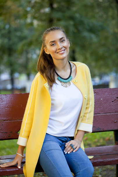Happy young woman in yellow coat in autumn street - Fotoğraf, Görsel